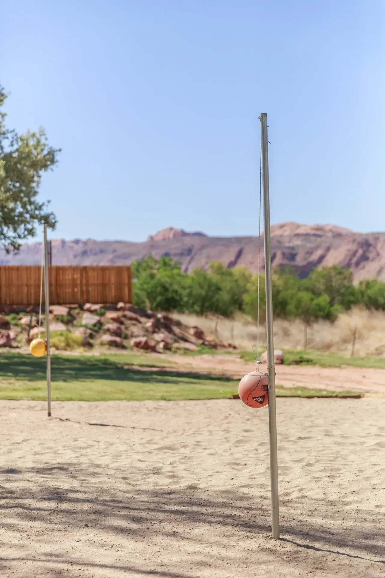 A volleyball game is being played on a sandy court with mountains in the background.