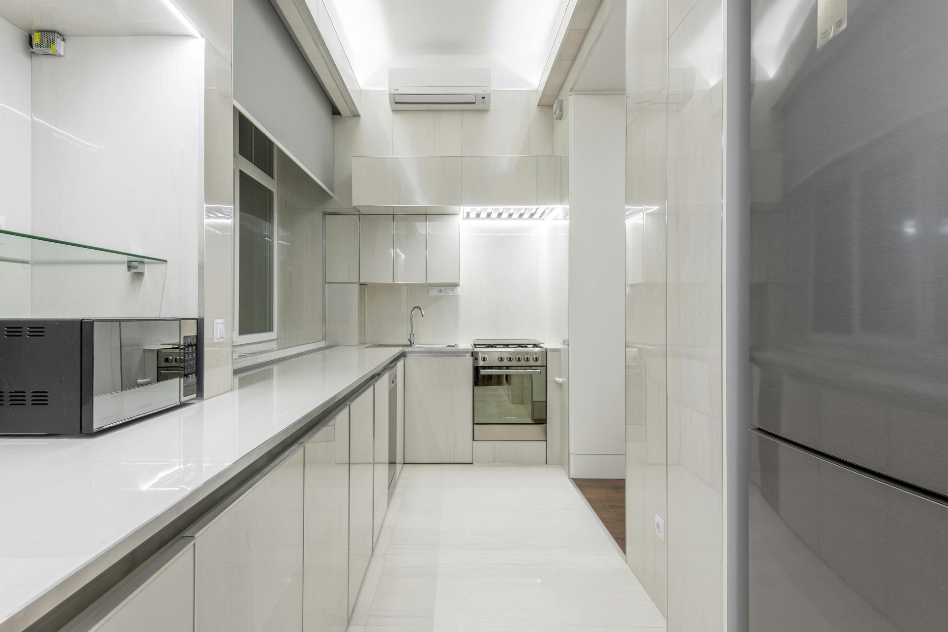 Bright modern white galley kitchen with glossy cabinets, island counter, and built-in appliances