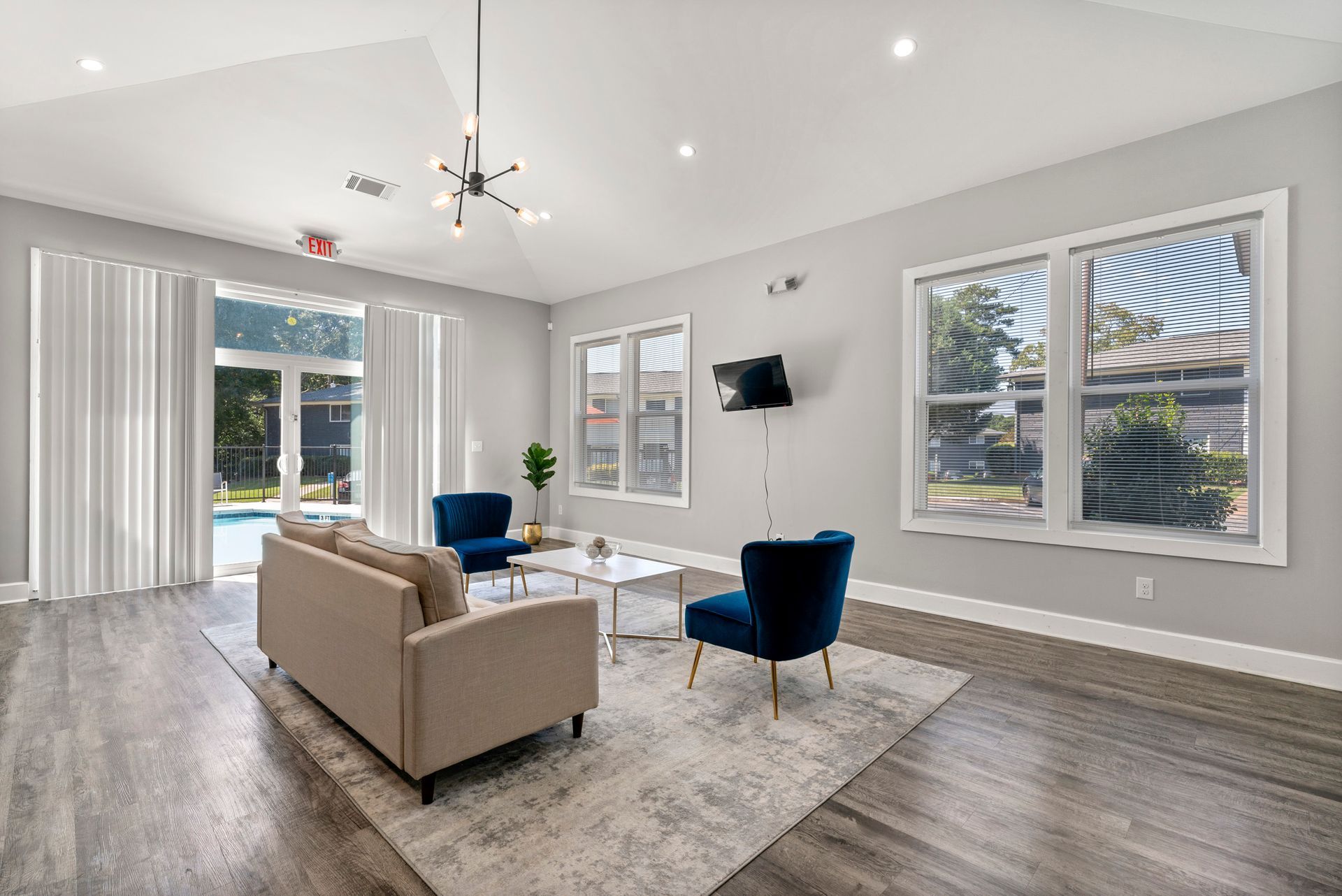 Bright modern living room with beige sofa, blue chairs, large windows, and wall-mounted TV