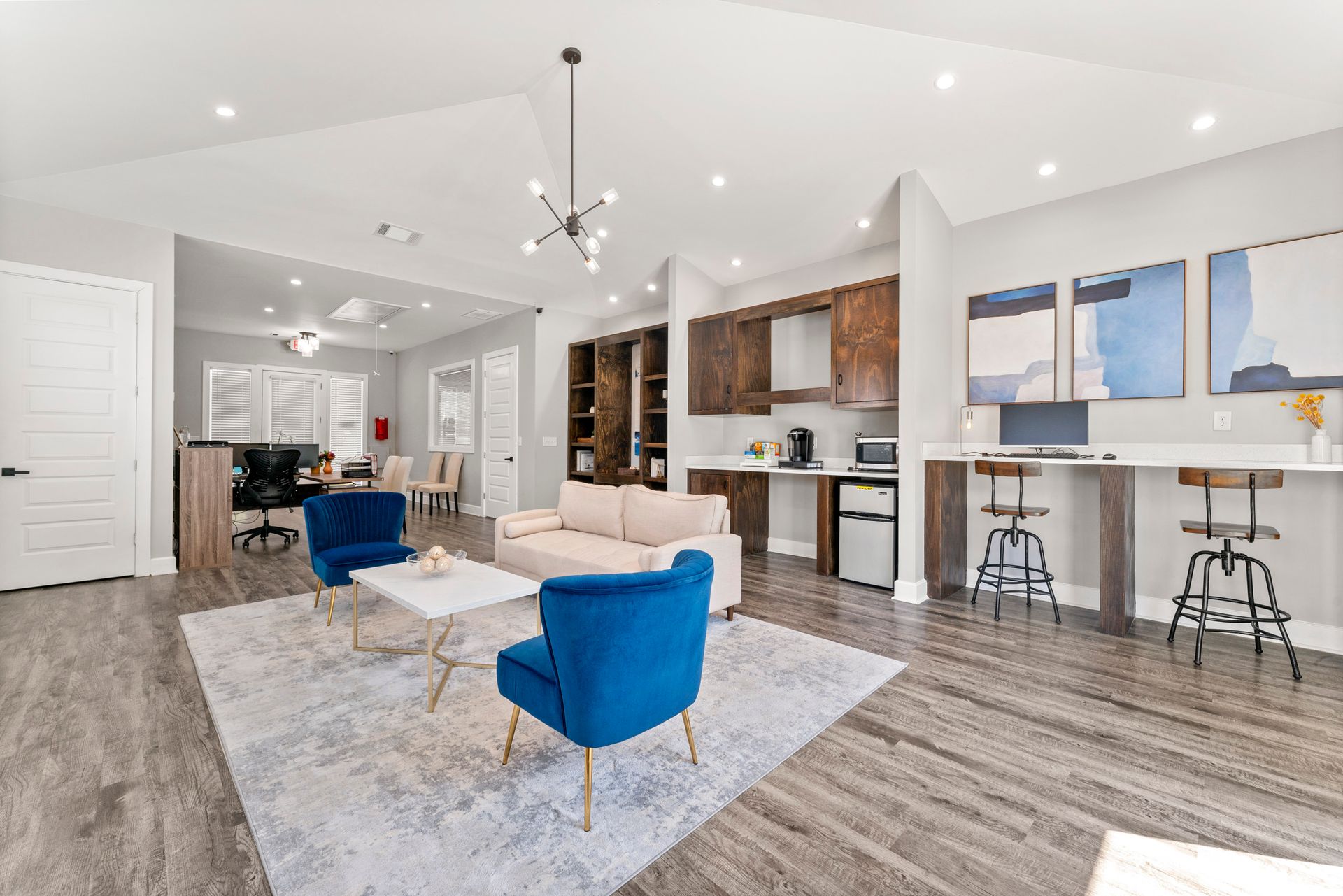 Bright open-concept living room and kitchen with blue chairs, white walls, and wood flooring