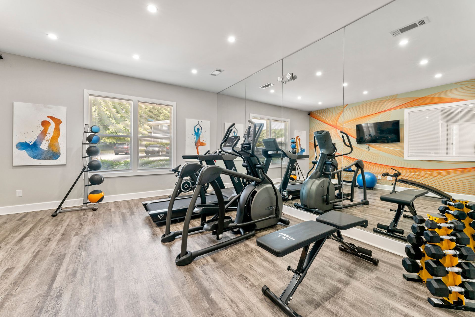 Modern gym with cardio machines, dumbbells, and bright wall art in a clean studio space