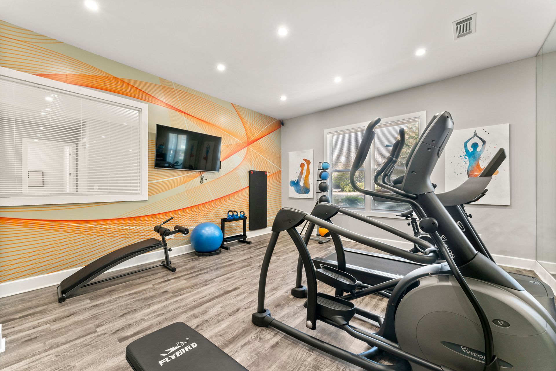 Home gym with treadmill, elliptical, TV, stability balls, and orange accent wall