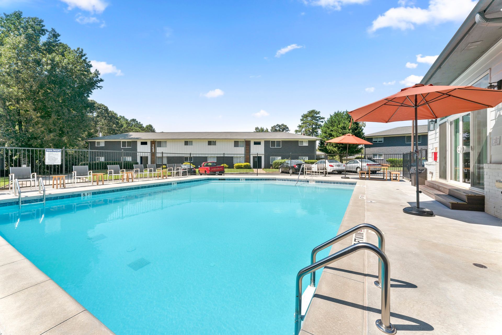 Outdoor swimming pool with clear blue water, lounge chairs, and an orange umbrella at an apartment complex