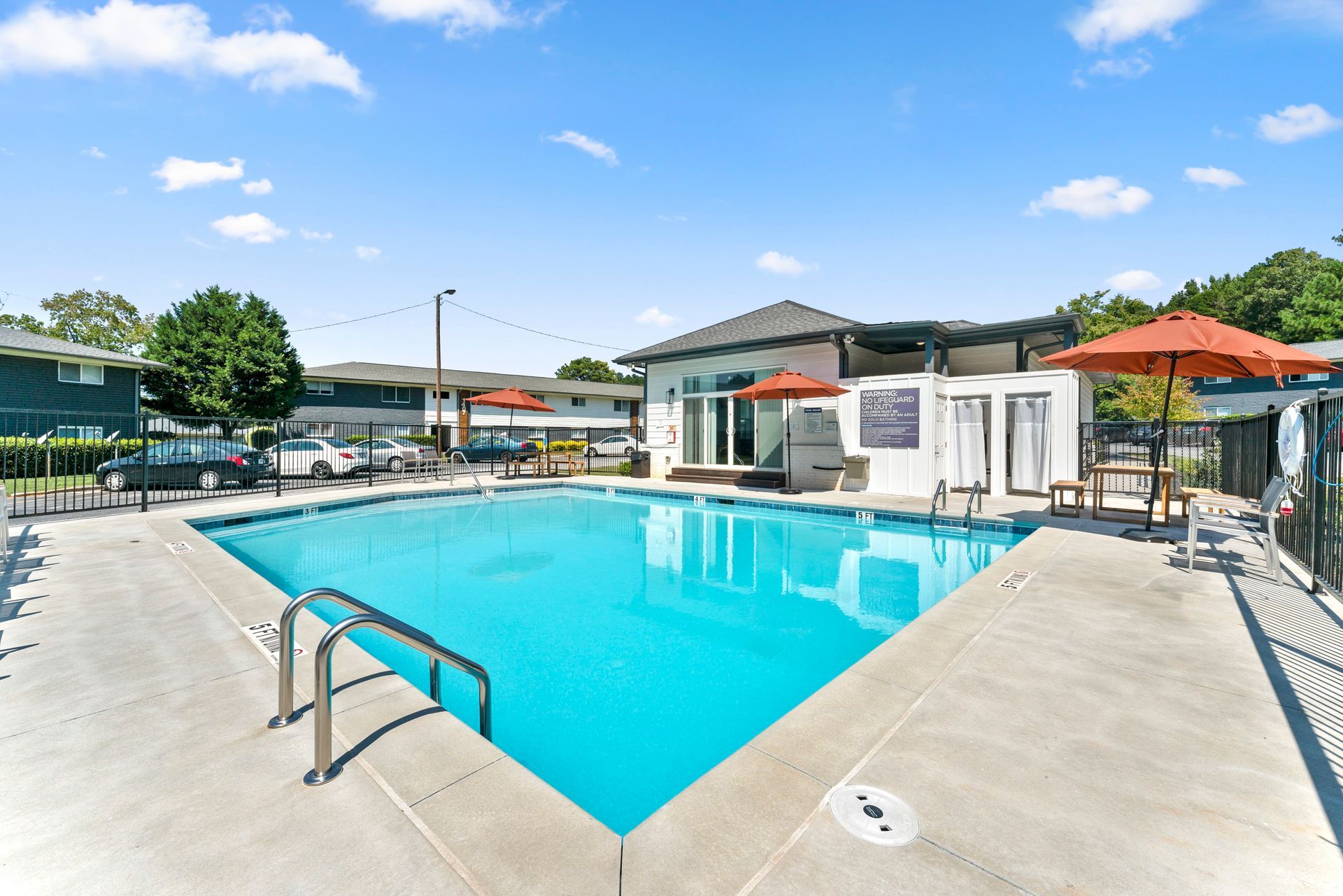 Outdoor swimming pool with blue water, lounge chairs, and orange umbrellas on a sunny day