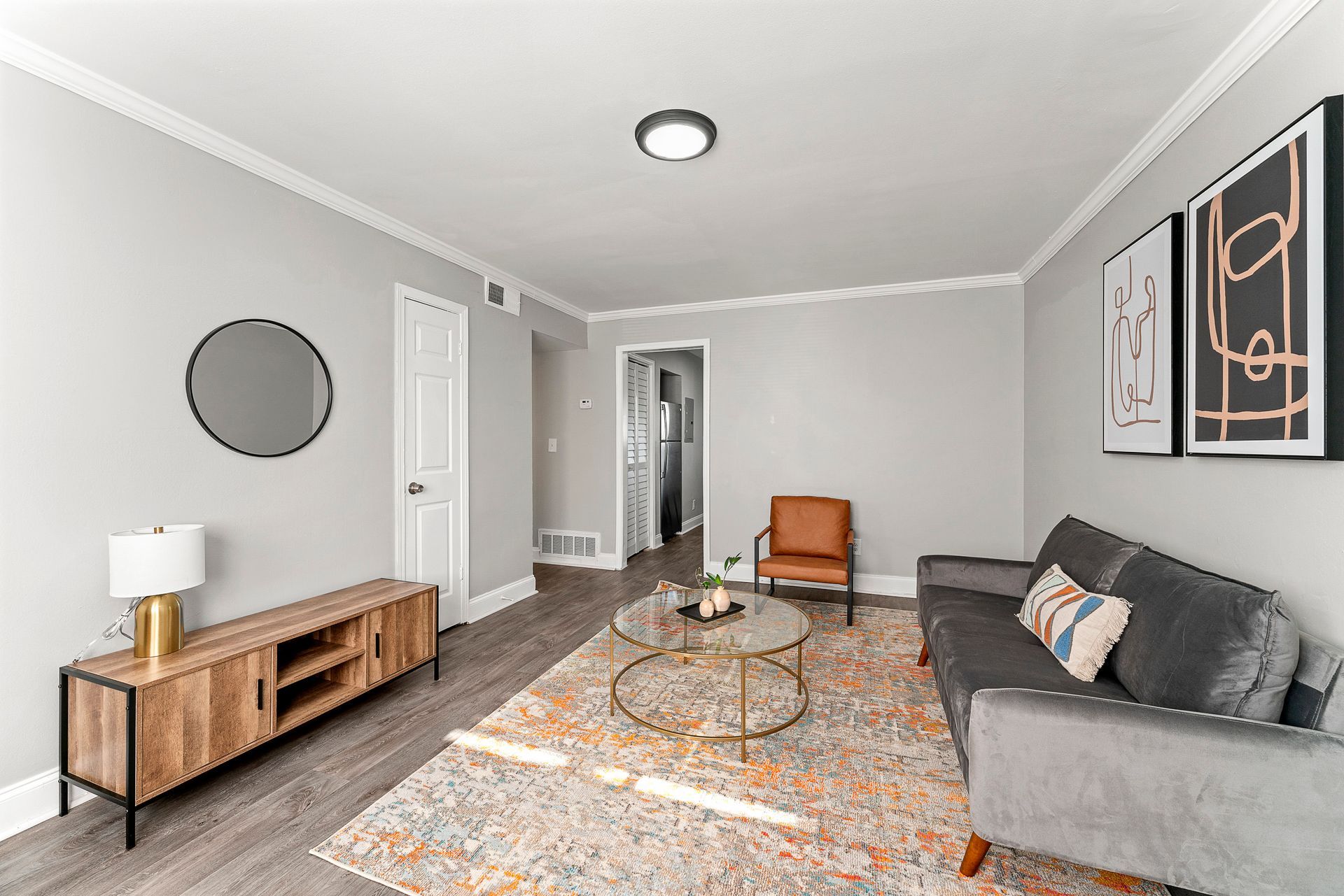 Modern living room with gray sofa, wooden TV console, round coffee table, and patterned rug on light gray walls.