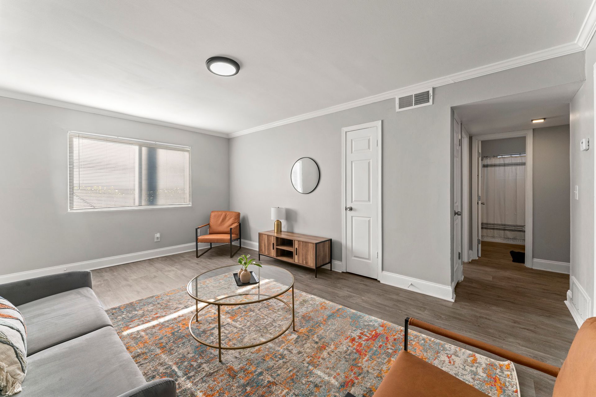 Bright gray living room with sofa, orange chair, round coffee table, patterned rug, and hallway entrance