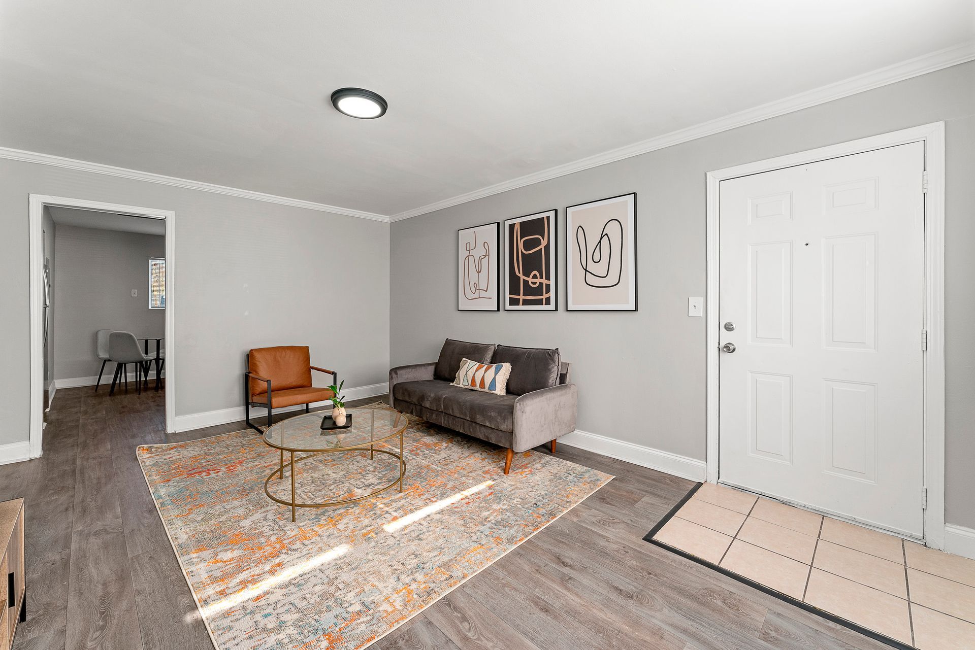 Modern living room with gray walls, gray sofa, patterned rug, wall art, and tiled entryway.