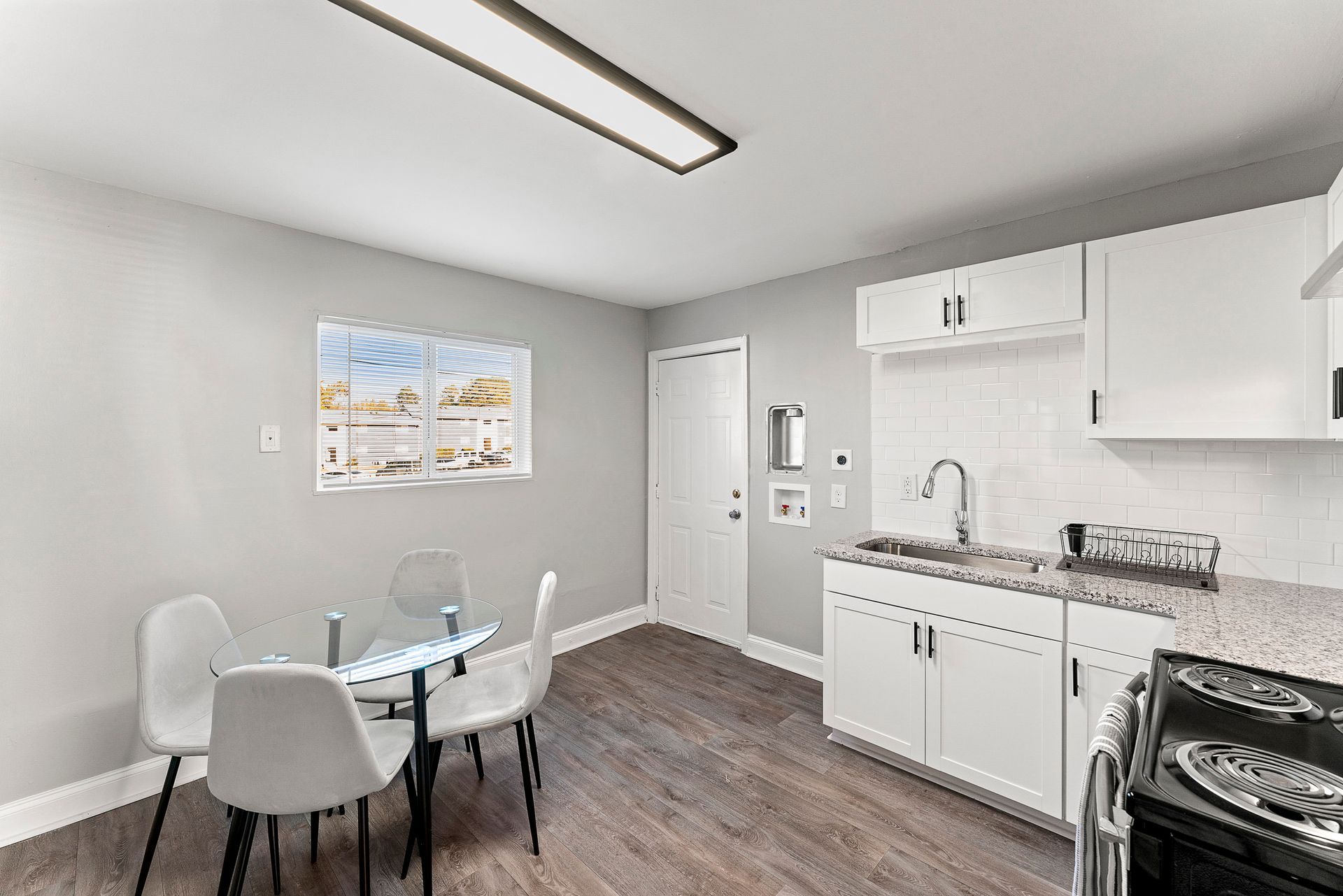 Bright dining nook with glass table, white chairs, and adjacent white kitchen cabinets and stove