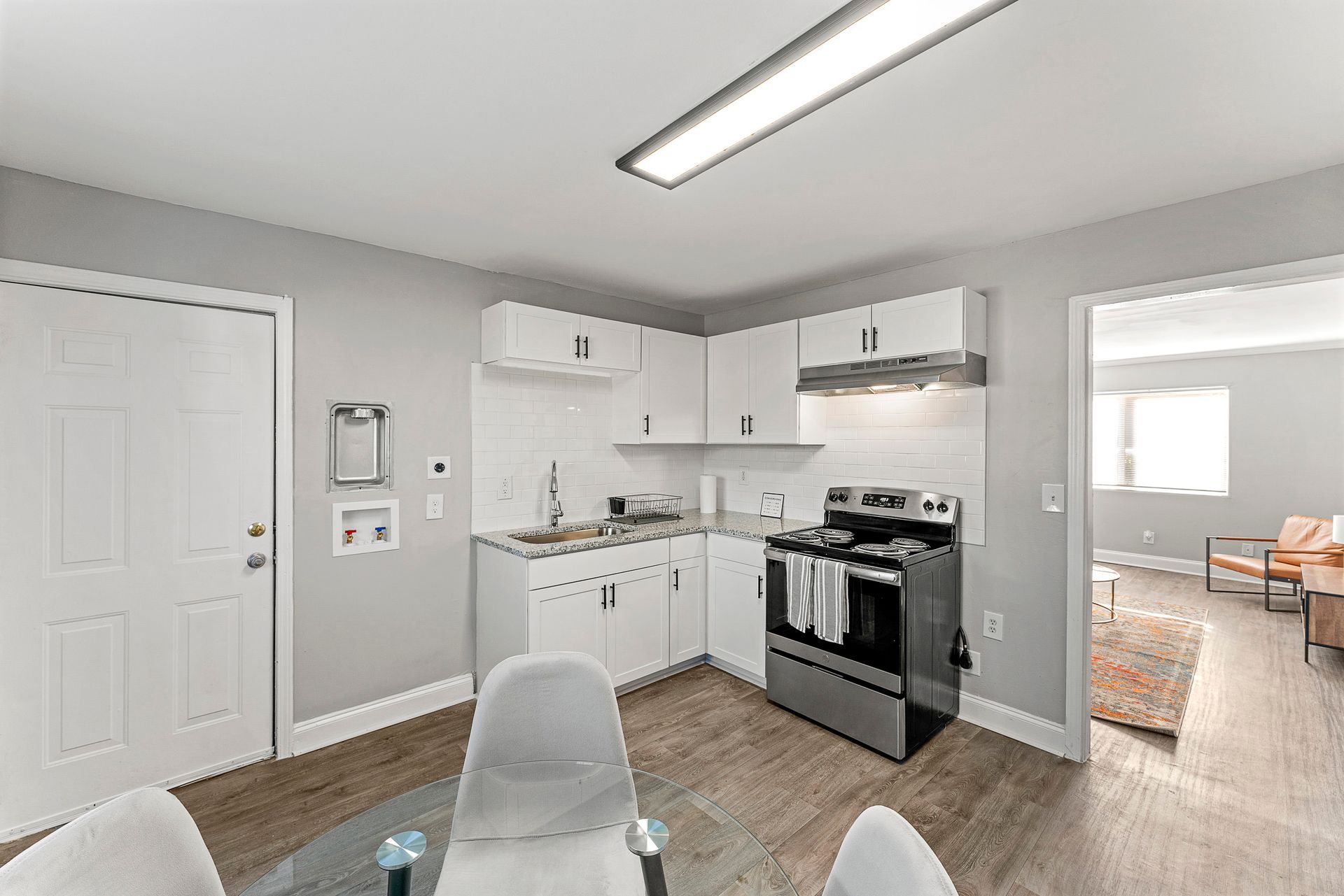 Small gray kitchen with white cabinets, stainless stove, and a doorway to a sunlit dining room