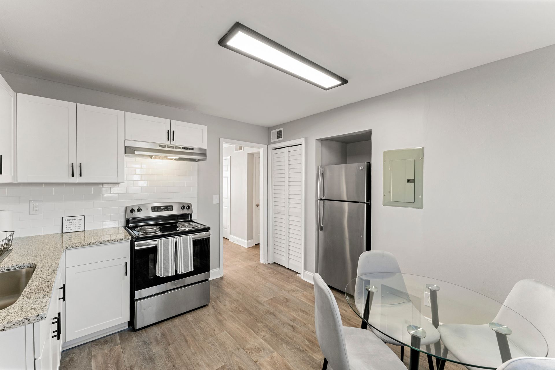 Bright modern kitchen with white cabinets, stainless stove and fridge, glass dining table, and wood floors.