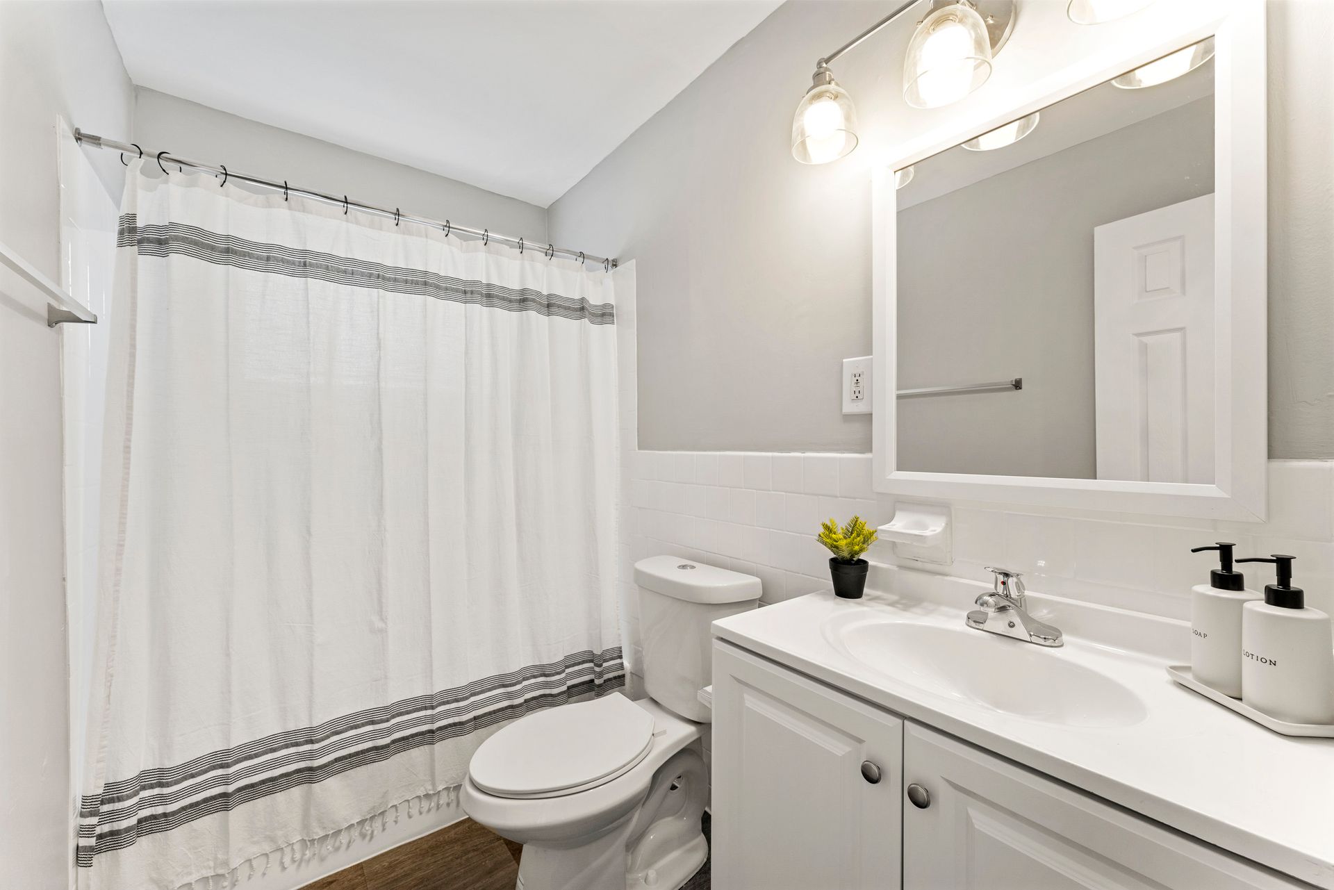 Bright bathroom with white shower curtain, toilet, vanity, mirror, and light gray walls