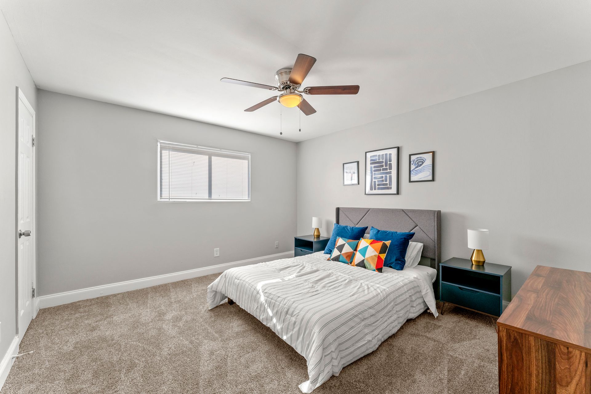 Bright bedroom with a bed, gray walls, ceiling fan, window, and wood dresser.