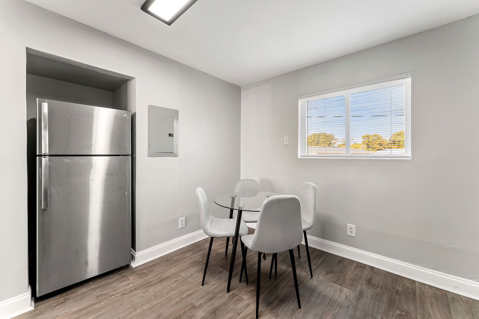 Small dining nook with stainless steel fridge, round table, four gray chairs, and a window.