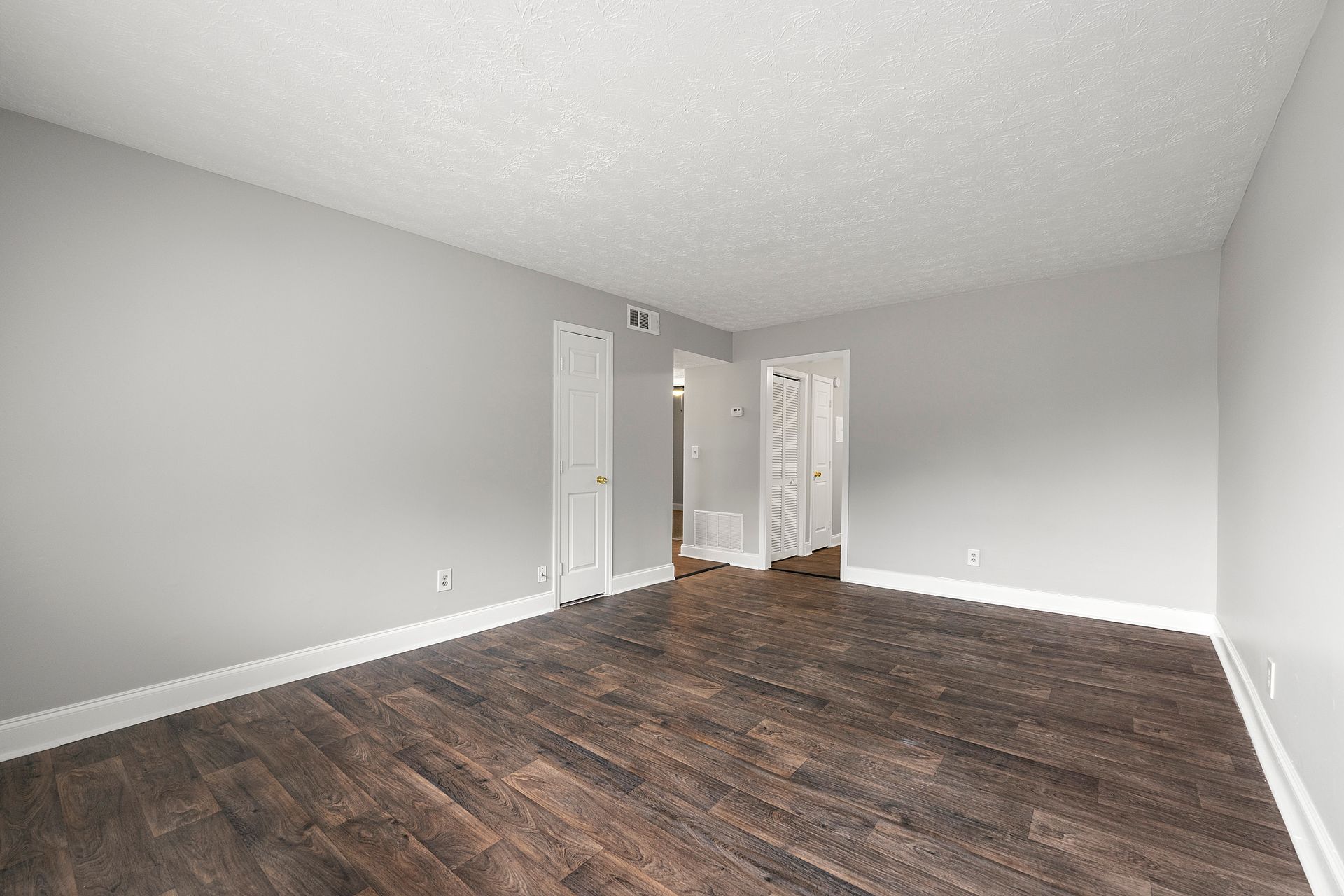 Empty gray room with dark wood floors, sloped ceiling, and two white doors.