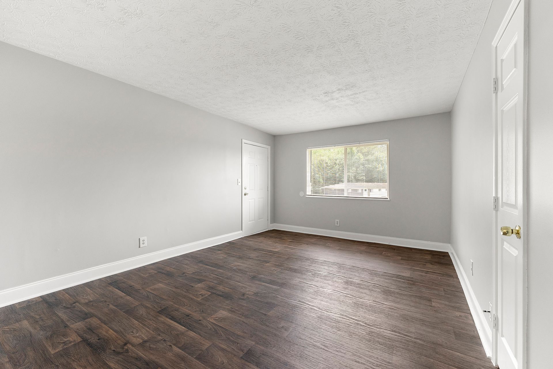 Empty gray bedroom with dark wood floors, white trim, a window, and a closed door
