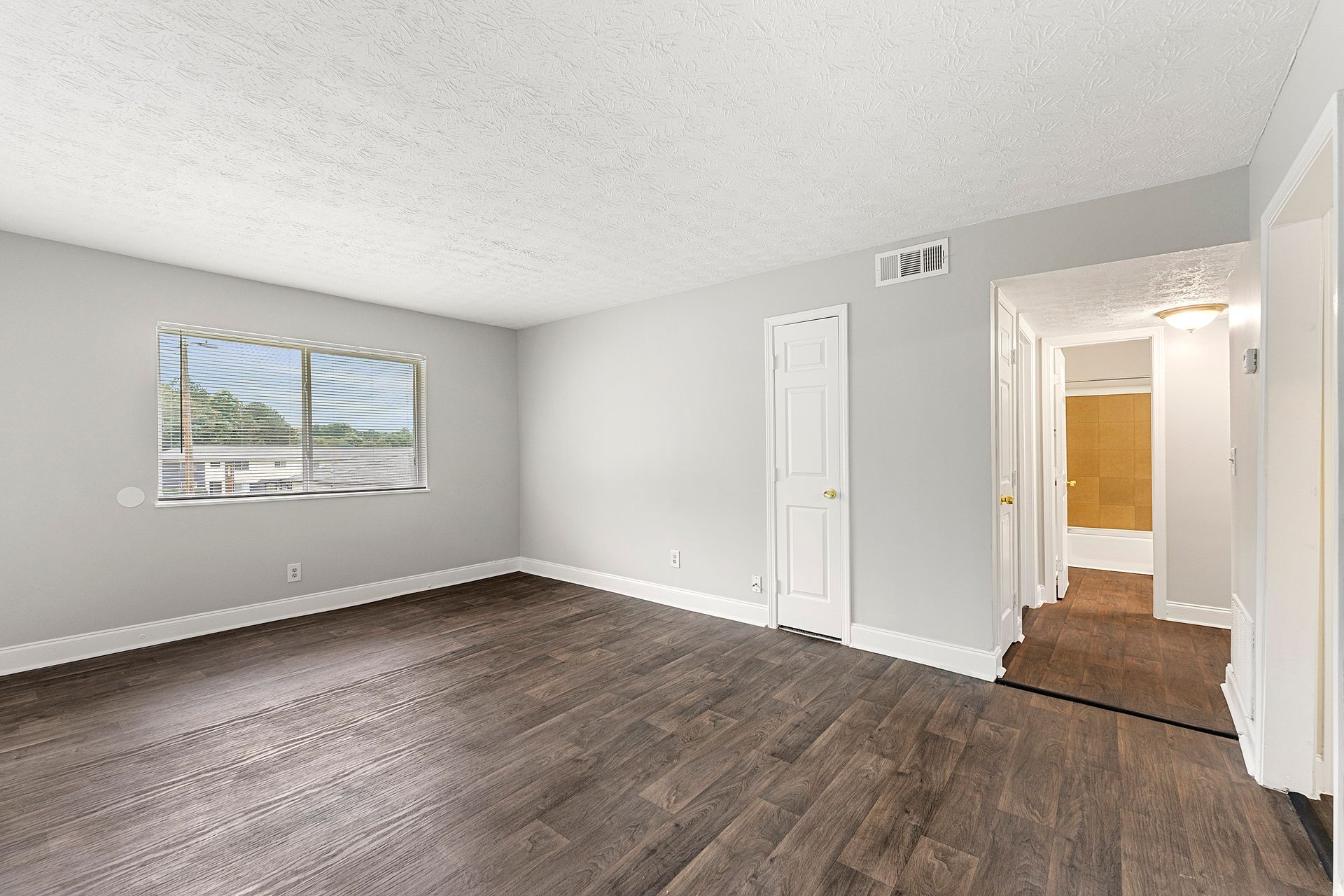 Empty gray room with dark wood floors, a window, and an open doorway to a hallway.