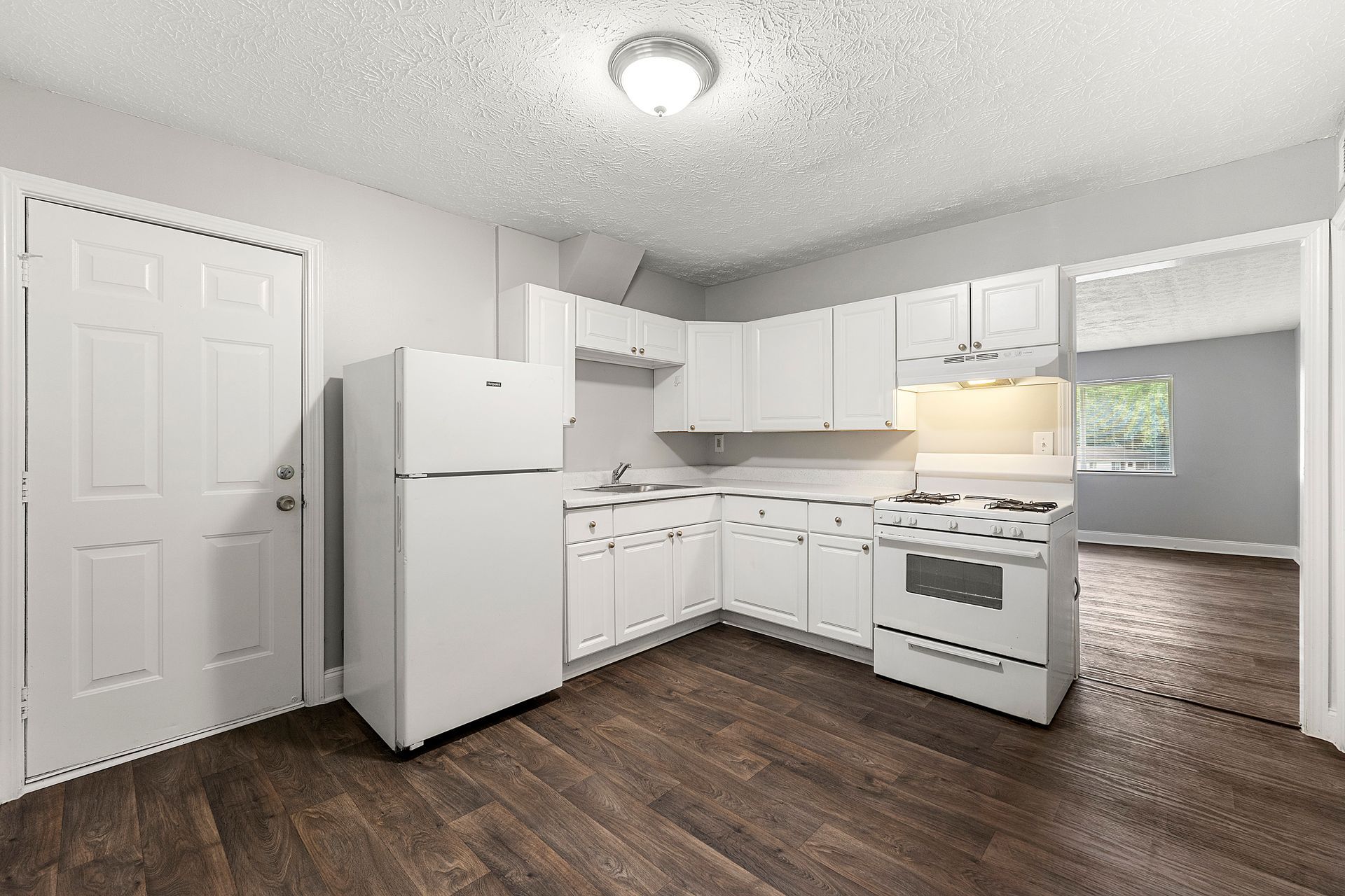 Empty white kitchen with cabinets, fridge, stove, and dark wood flooring