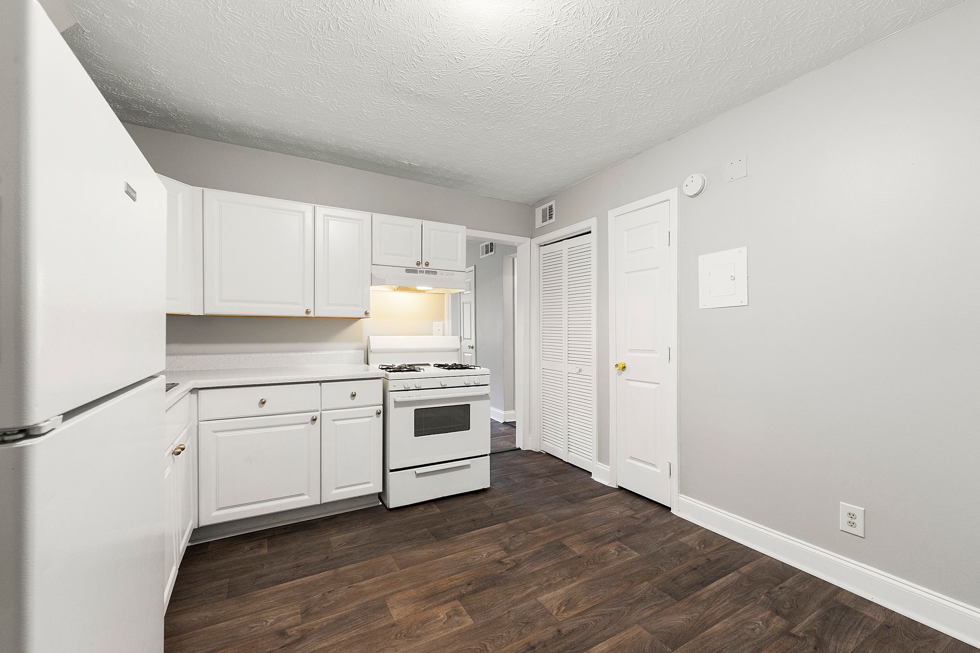Small white kitchen with stove, cabinets, refrigerator, and dark wood flooring