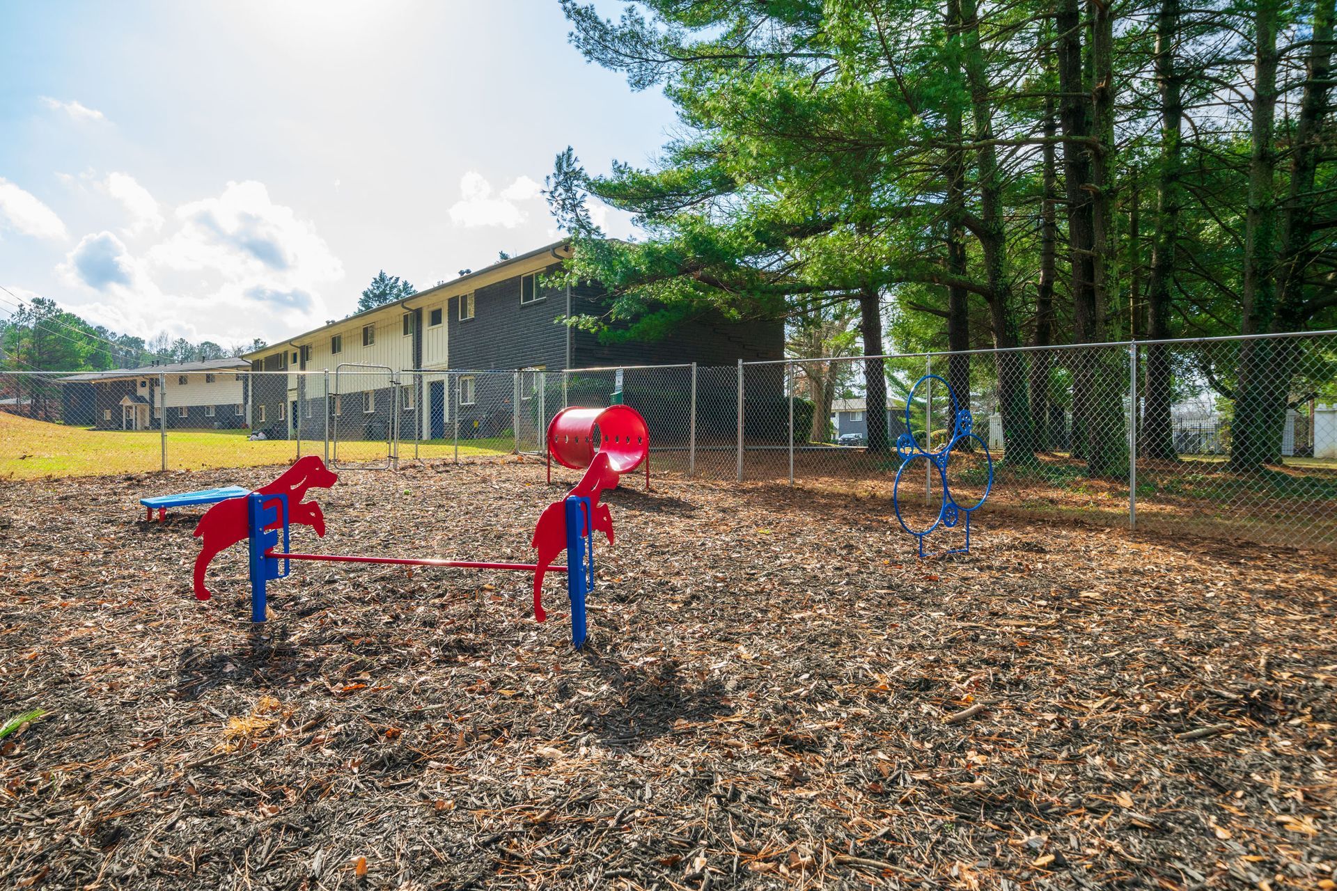 Colorful outdoor playground with red and blue climbing equipment on wood chips near trees and a building