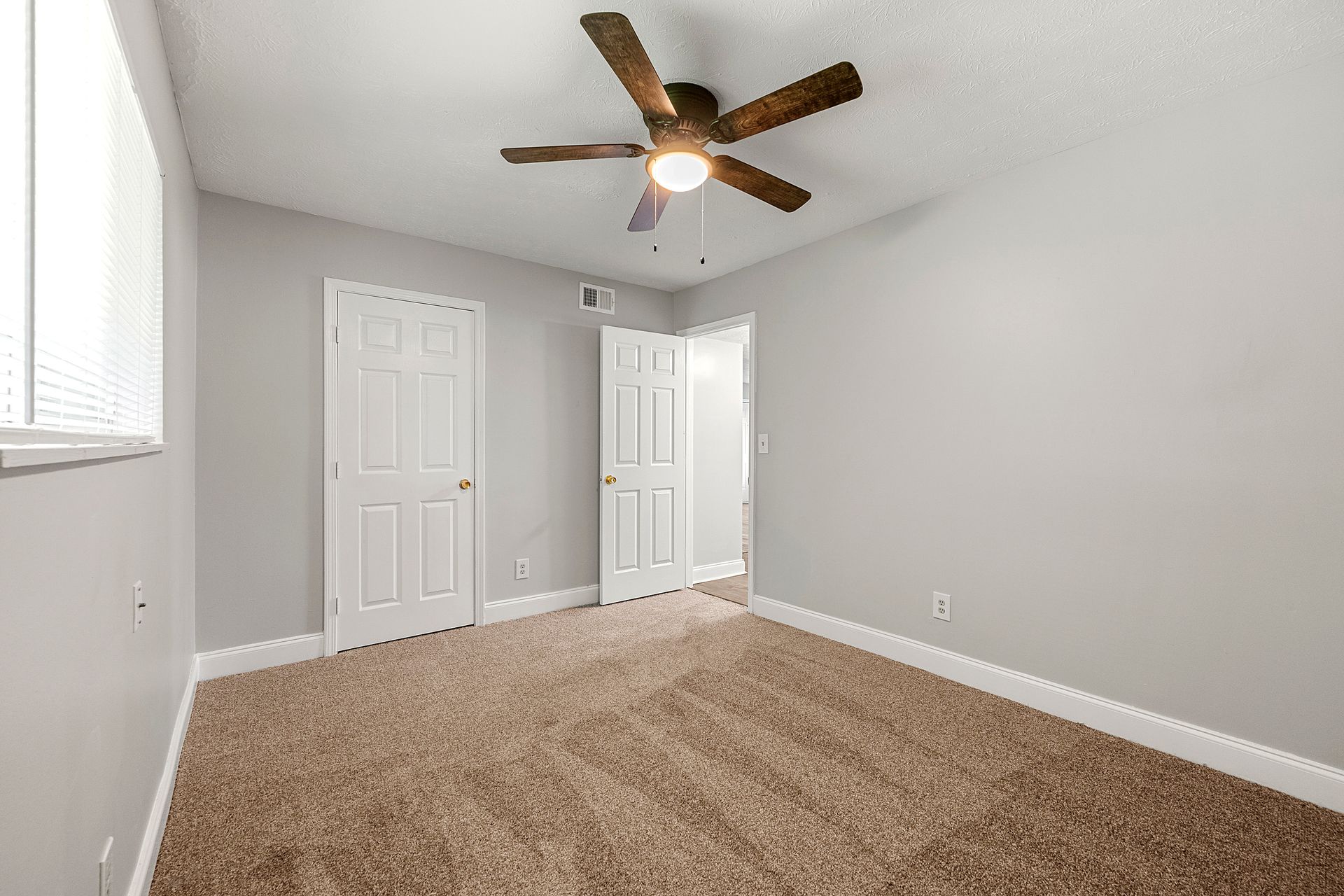 Empty gray bedroom with beige carpet, white doors, and a ceiling fan.