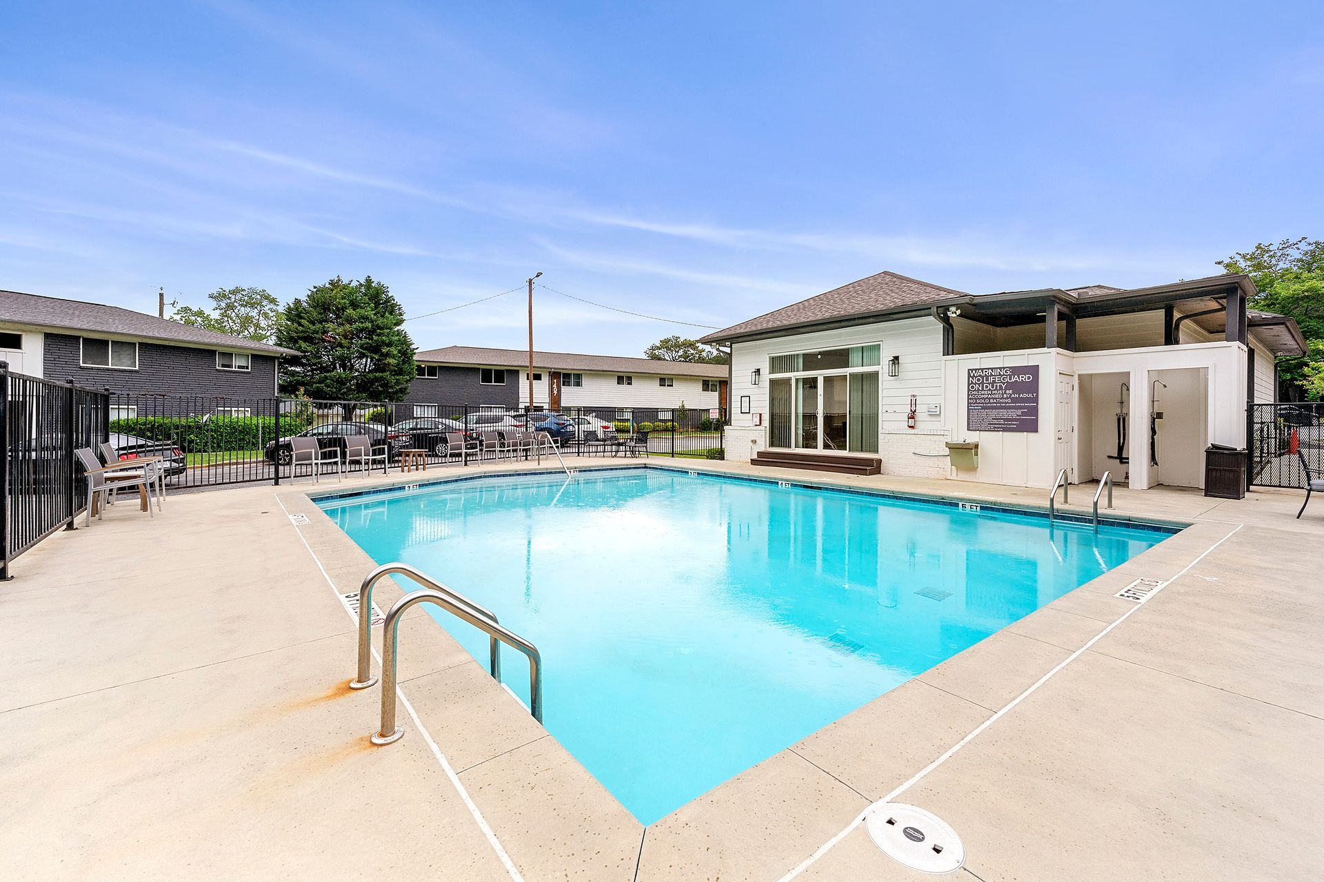 Outdoor swimming pool with bright blue water, beige deck, and apartment buildings surrounding it