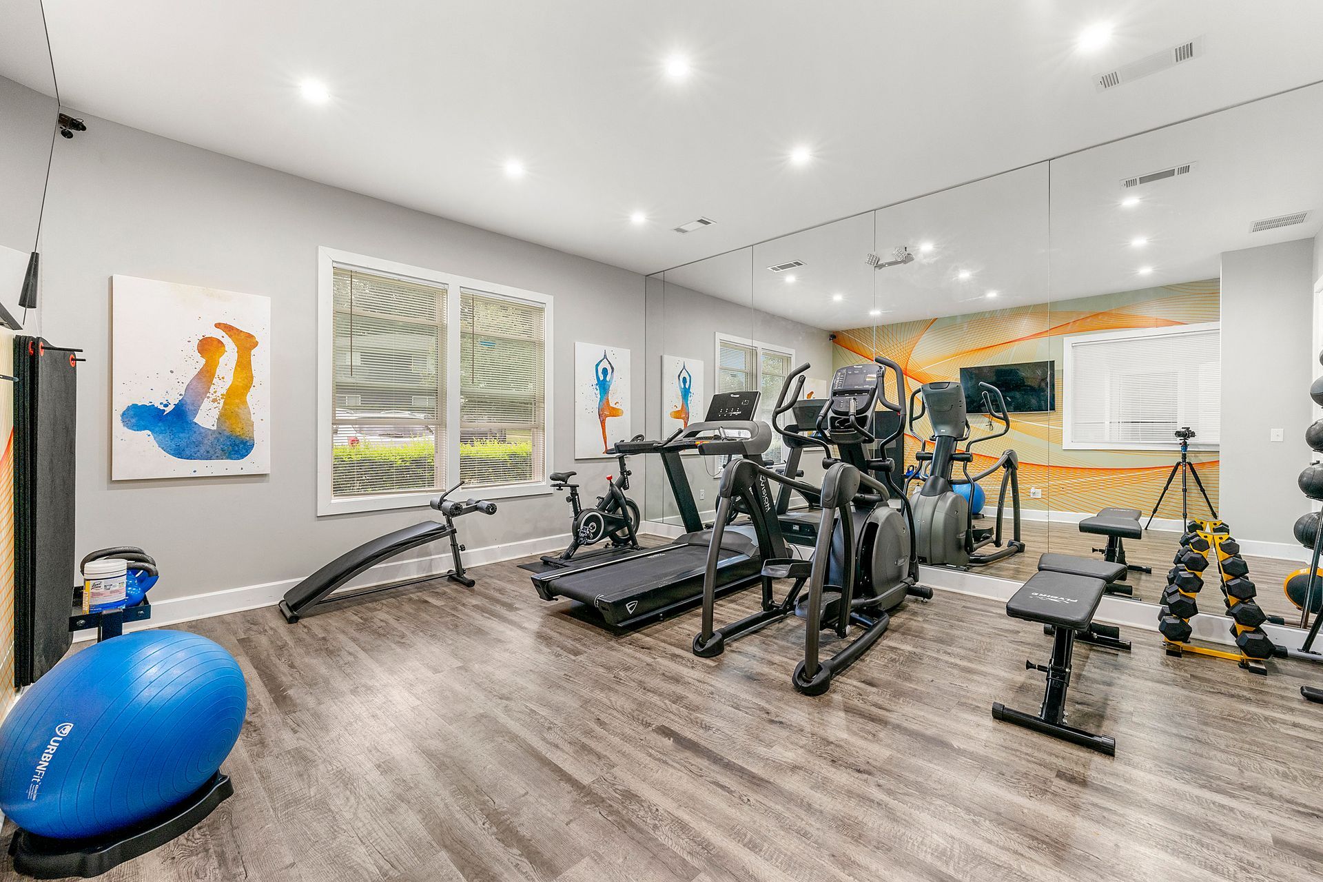 Bright modern gym with treadmills, weight benches, dumbbells, and exercise balls on wood flooring
