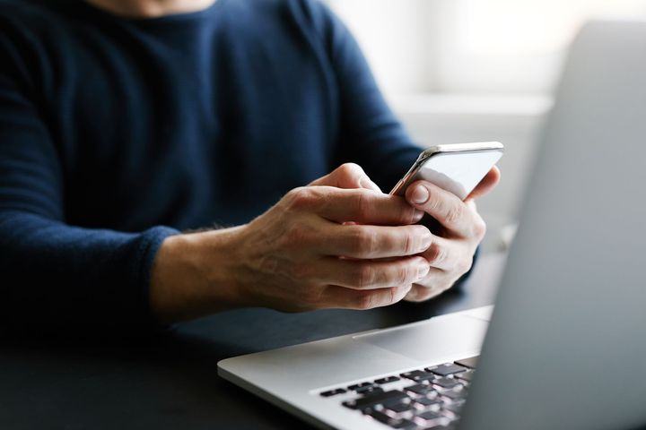 Hands holding a smartphone beside an open laptop on a desk