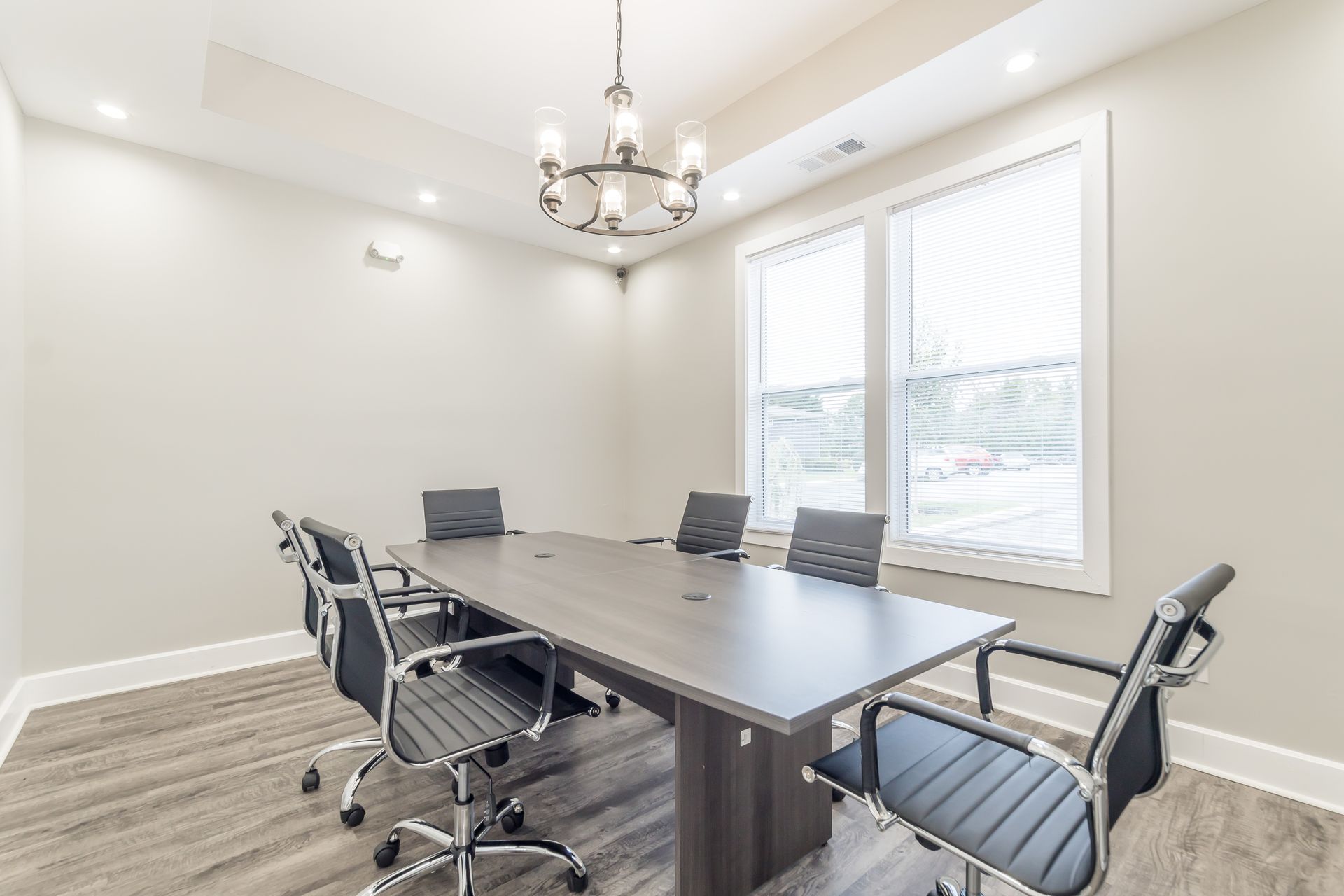 Modern conference room with gray table, black chairs, chandelier, and large windows with blinds