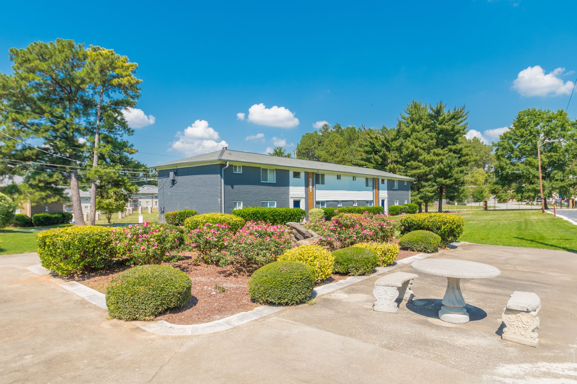 Small park pavilion with flower beds, benches, and trees under a bright blue sky