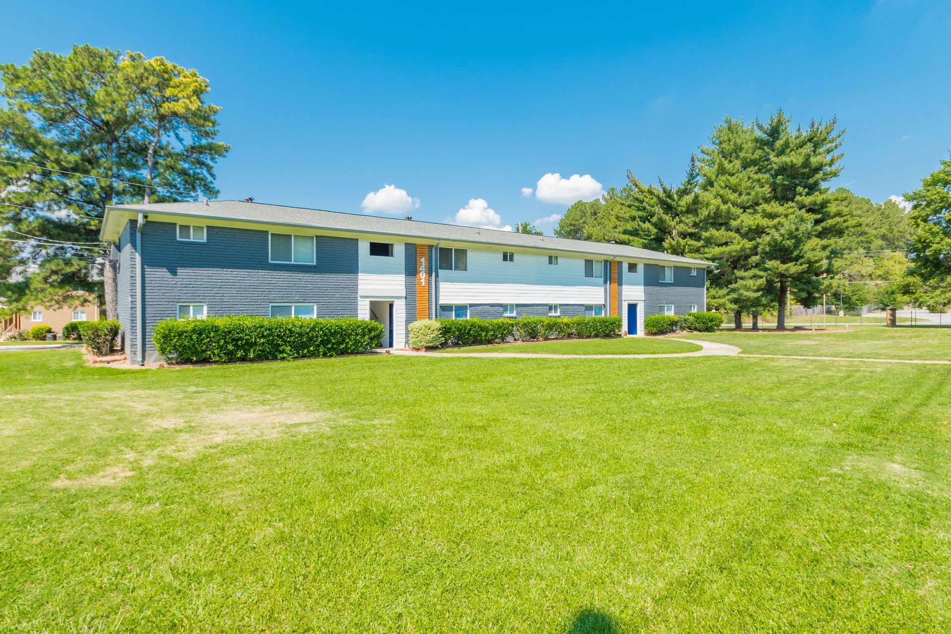 Blue apartment building with white trim beside a large green lawn on a sunny day