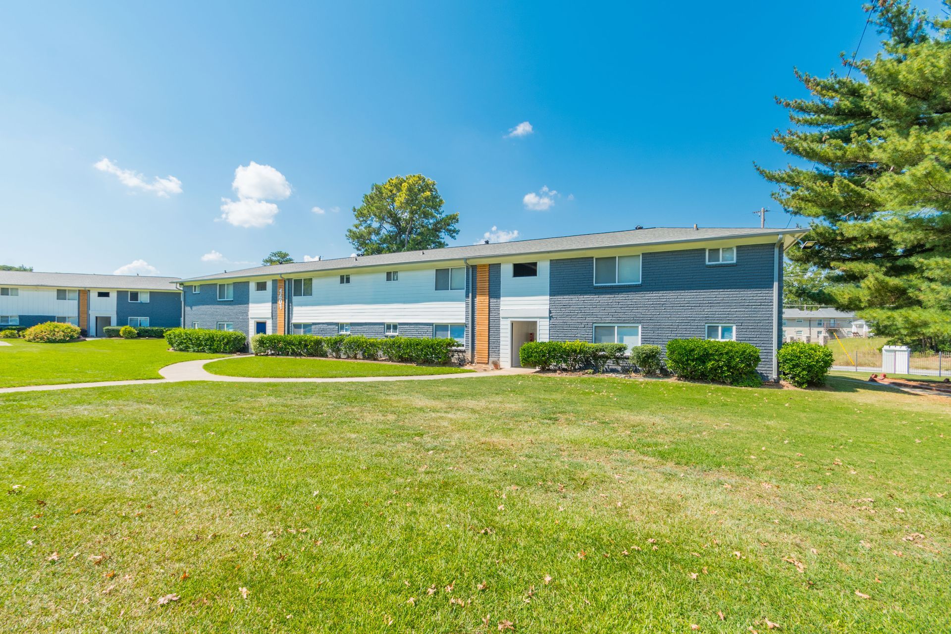 Sunny apartment complex with blue and white buildings and a green lawn under a clear sky