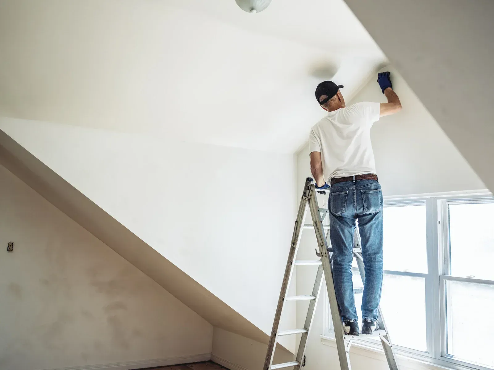 A man is standing on a ladder painting a wall.