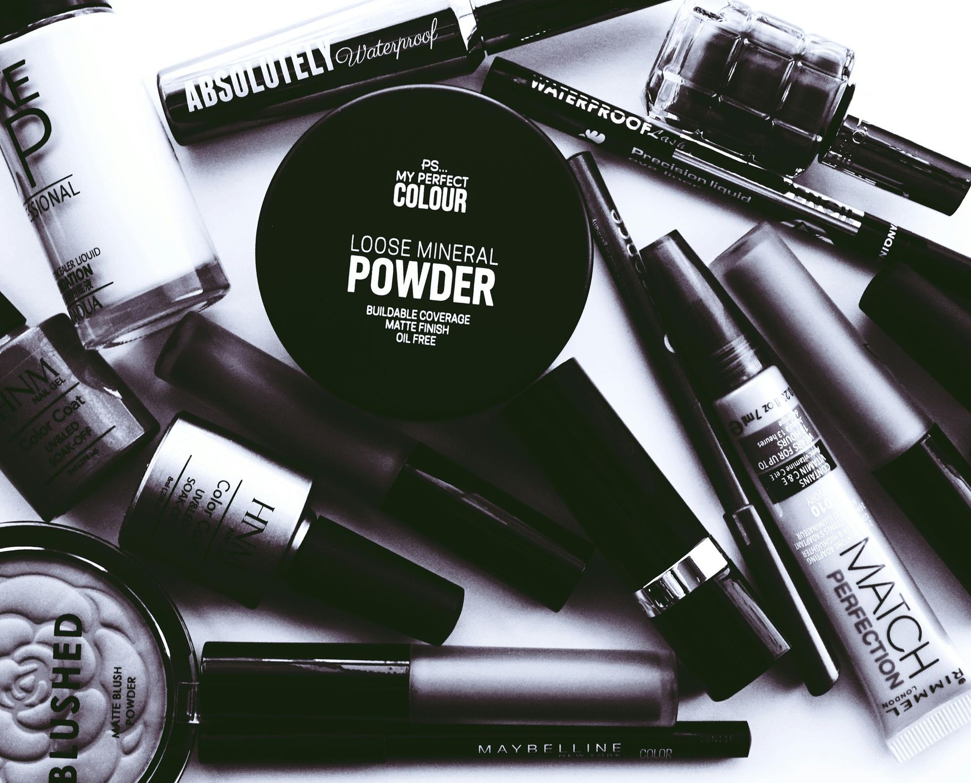 A mixed variety of cosmetics are sitting on a table in black and white.