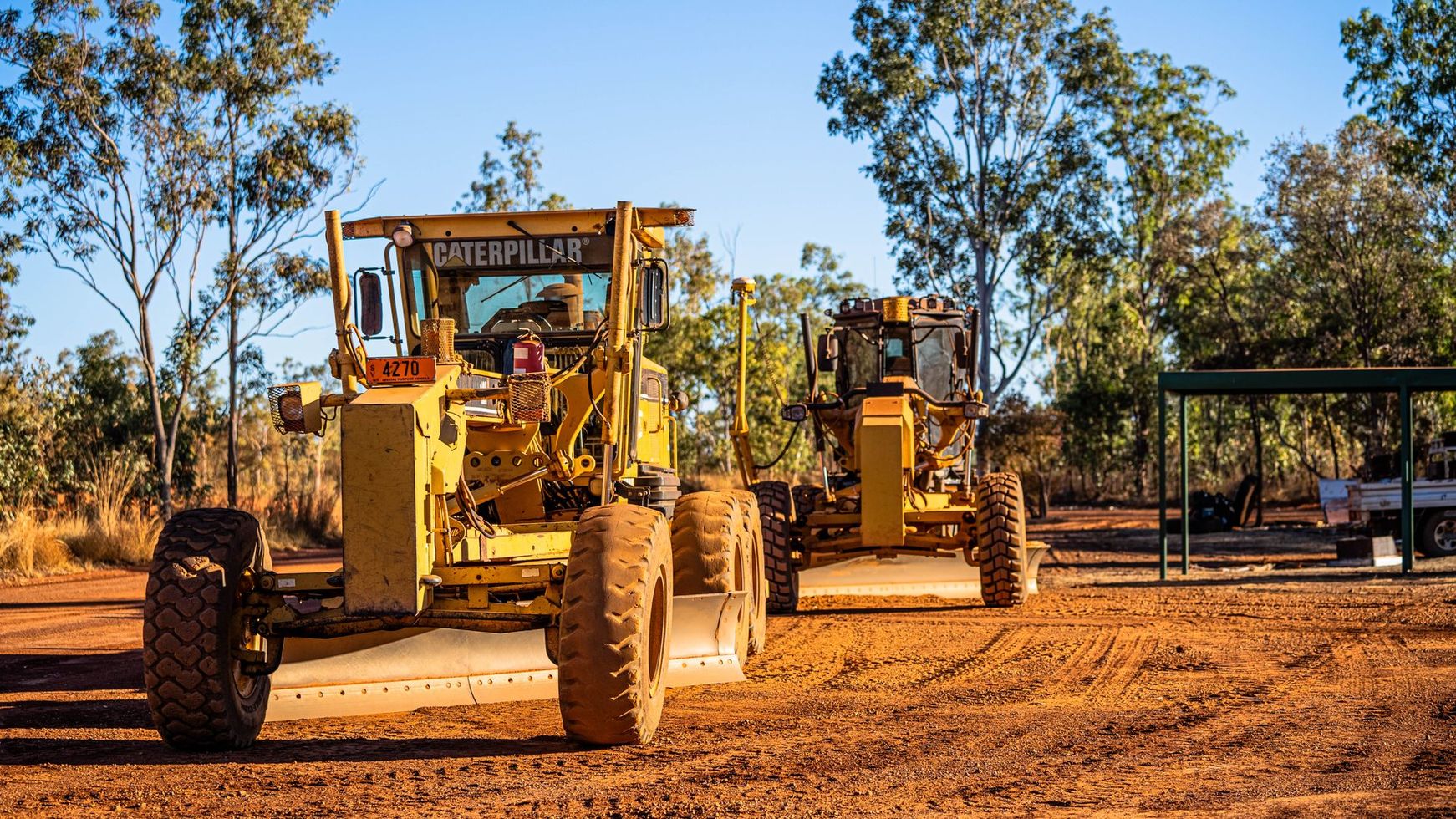 Two bulldozers are parked next to each other on a dirt road.