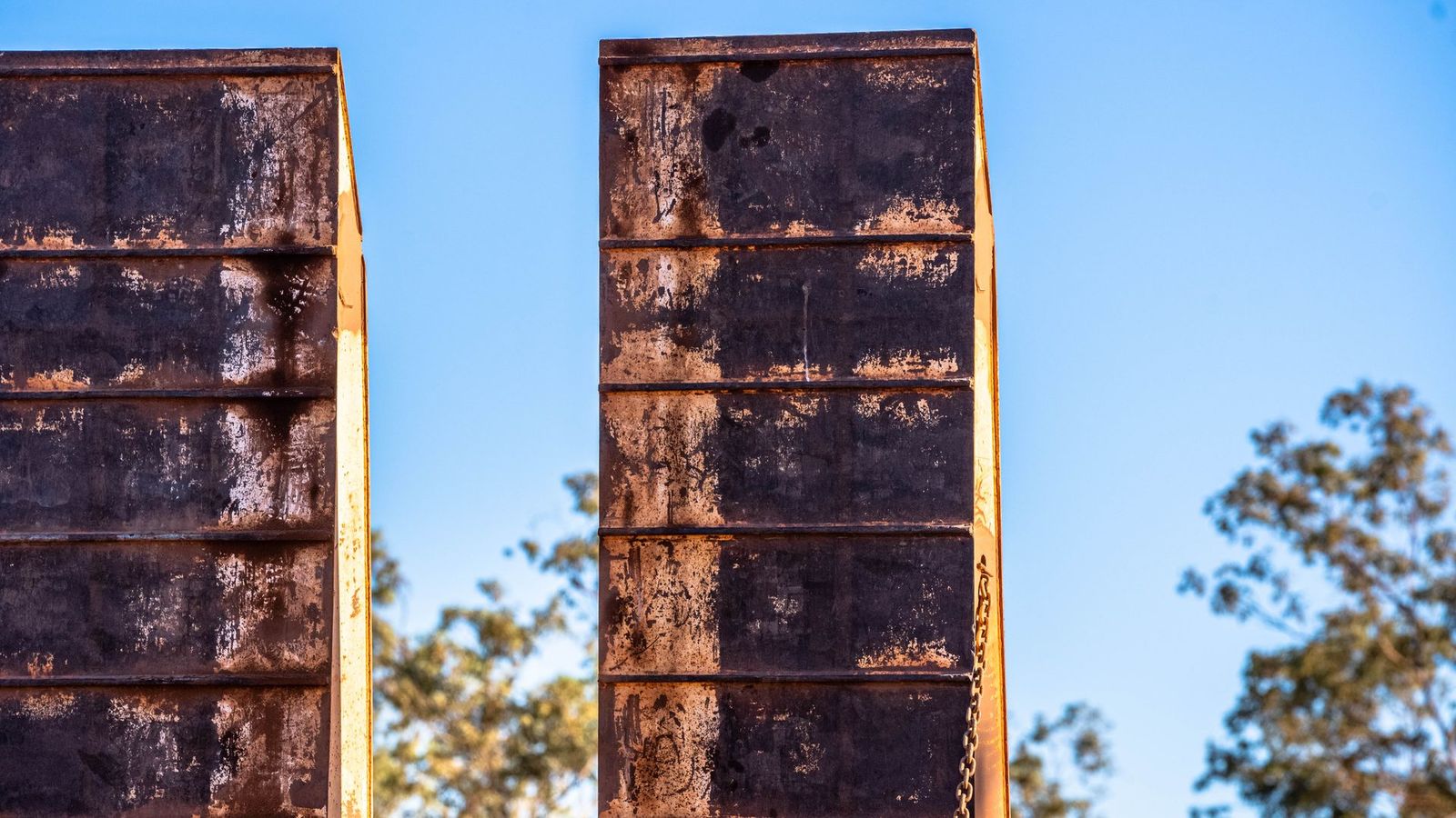 A close up of a rusty metal fence with trees in the background.
