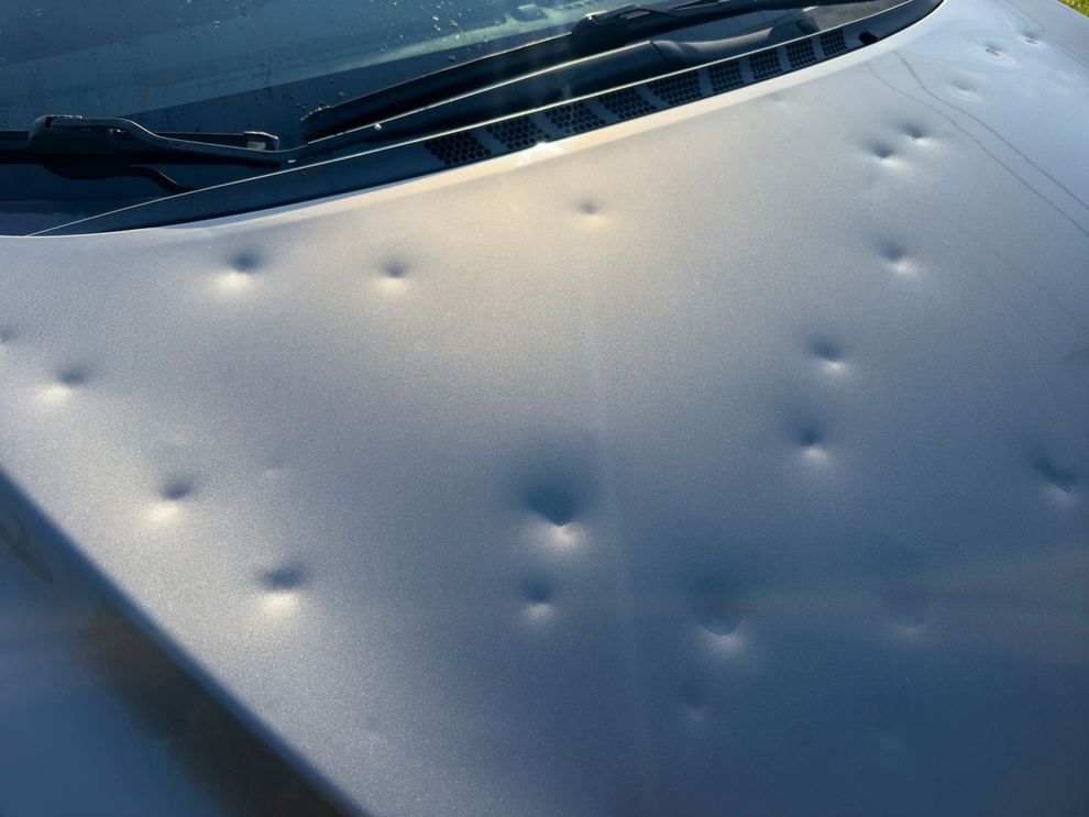 Cofano grigio di un'auto gravemente ammaccato dalla grandine.