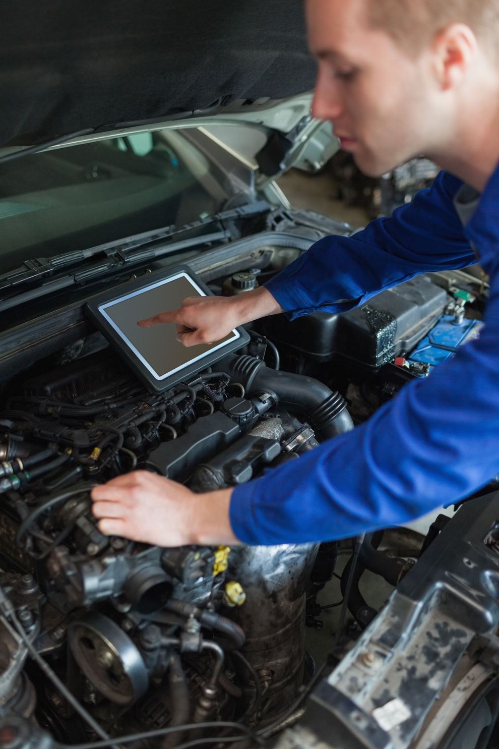 Meccanico in tuta blu che utilizza un tablet per diagnosticare il motore di un'auto.