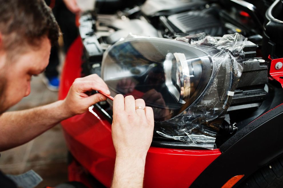 Uomo che applica la pellicola al faro rosso di un'auto con un attrezzo.