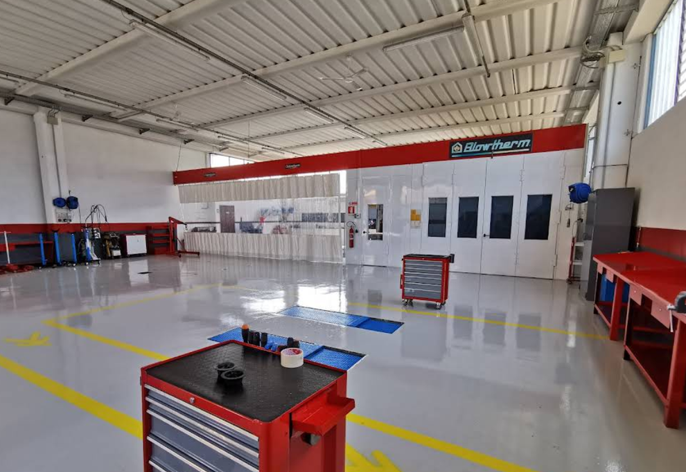 All'interno di un'officina di riparazione veicoli con cabina di verniciatura. Edificio rosso e bianco con attrezzi e attrezzature.