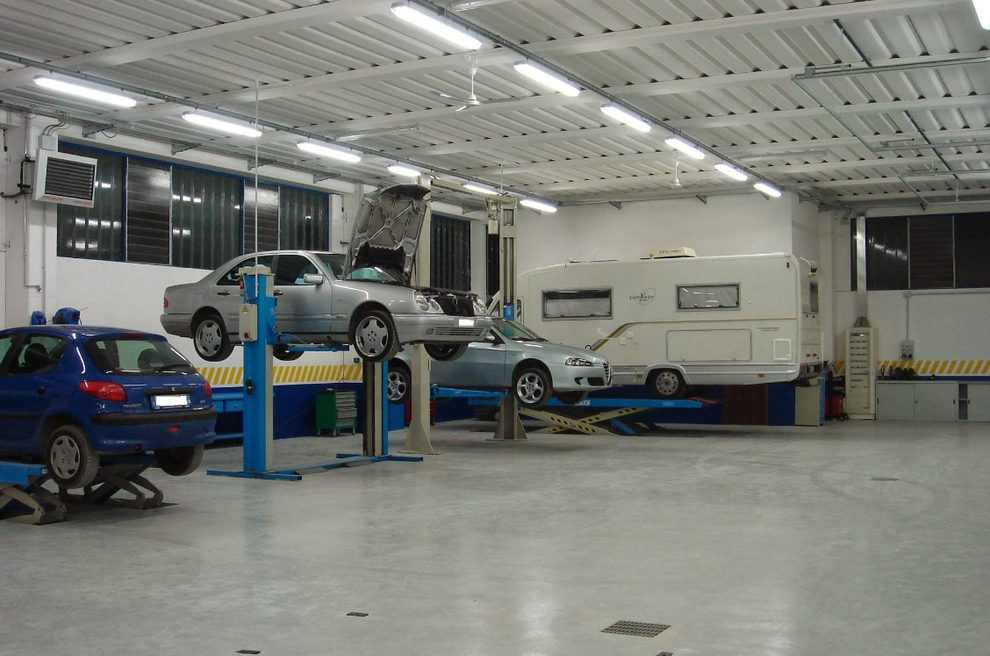 Auto e un camper su ascensori in un garage. Veicoli blu e argento. Illuminazione fluorescente.