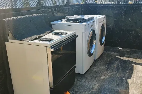 White stove, washer, and dryer in a dark-colored truck bed, possibly for disposal or transport.