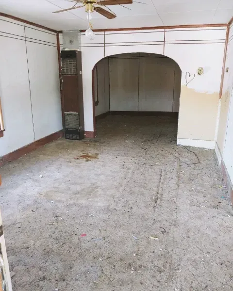 Empty room with dirty floor and damaged walls, archway to another room.