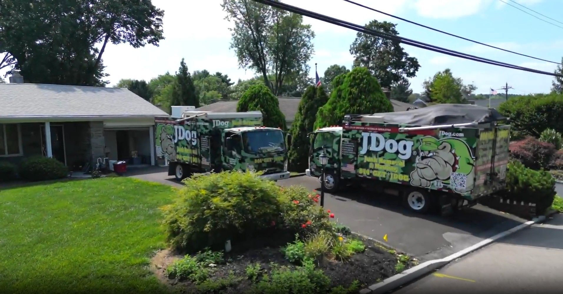 Two JDog junk removal trucks parked in front of a house, driveway, and lawn.
