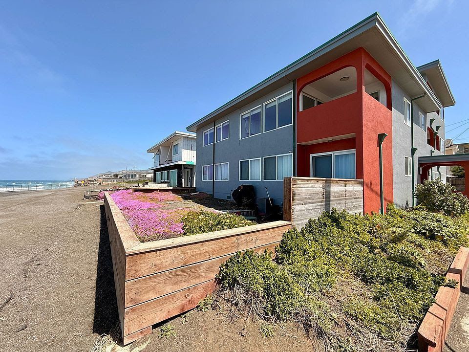 Oceanfront fourplex at 1 Paloma Avenue in Pacifica, CA, with a red and gray three-story facade above the beach