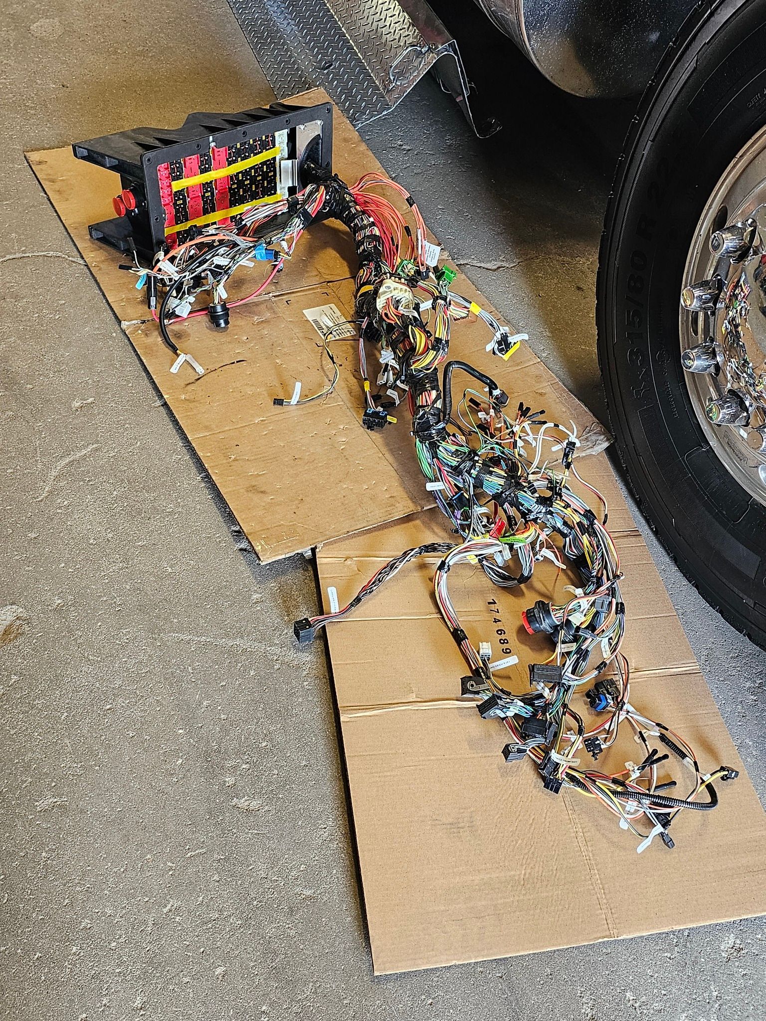 Cardboard spillway with colorful candy flowing across pavement beside a car tire and a small toy gate.