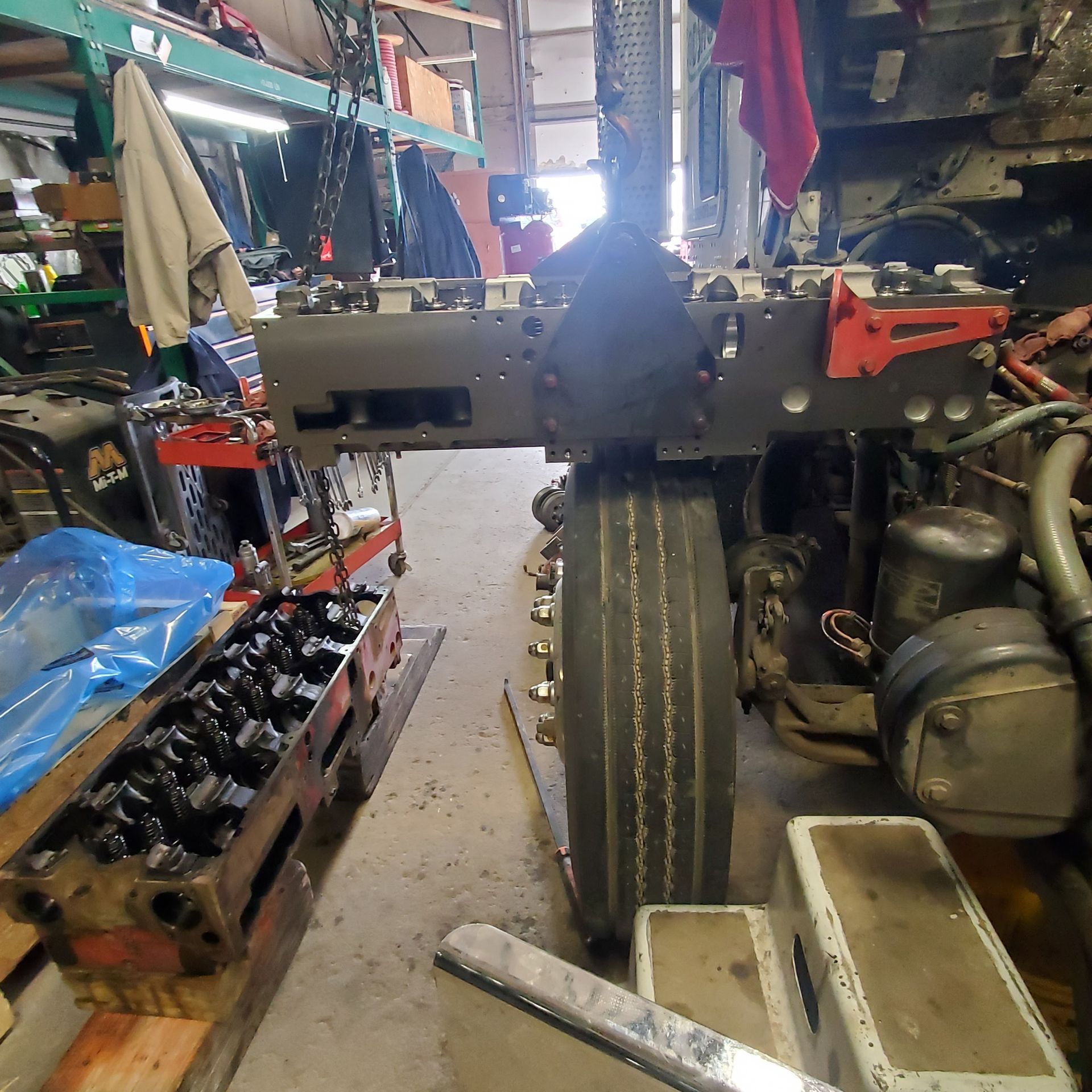 Garage with a vehicle chassis, front tire centered, engine parts and tools scattered around.