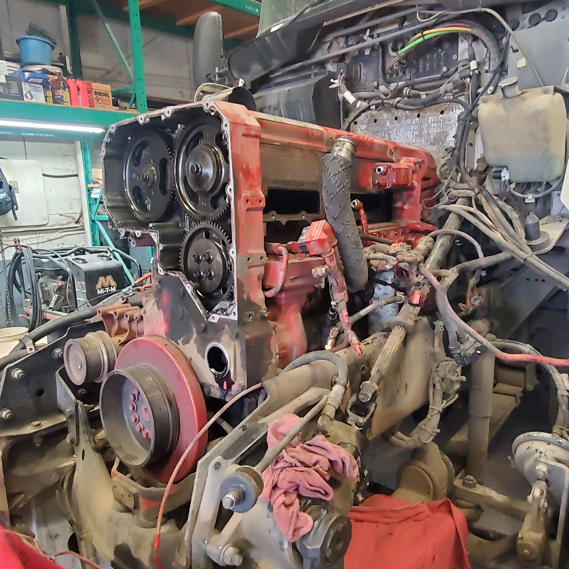 A cluttered auto shop with an exposed engine block and assorted engine parts on a workbench.