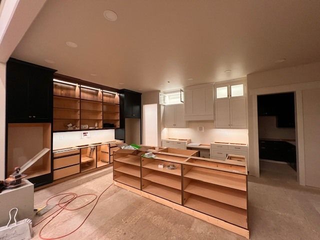 Kitchen renovation in progress, featuring unfinished cabinets, island, black and white cabinets, and overhead lighting.