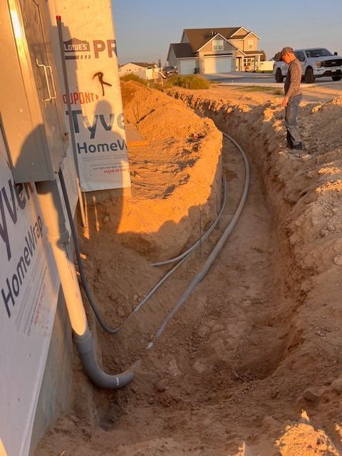 Electrical conduit in trench, near a house under construction. A person is near the trench.