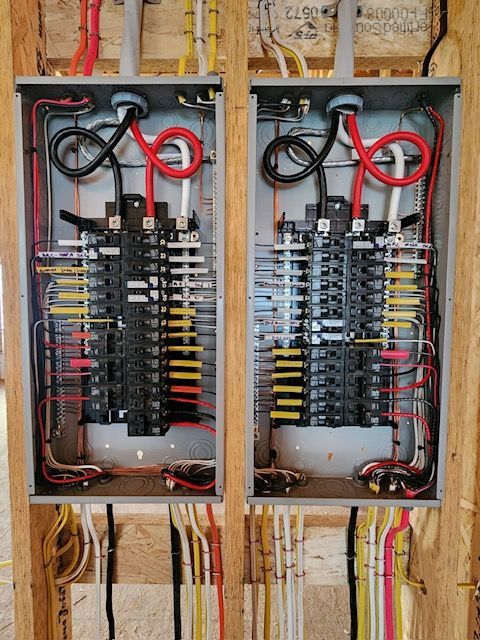Two electrical panels with numerous wires of various colors, installed in a wooden frame.
